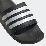 Black Adidas slide sandal with three white stripes on a light gray background